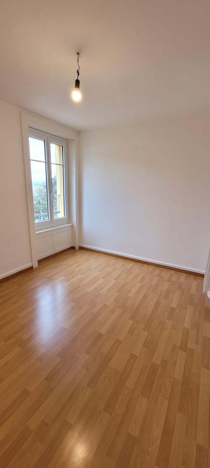 Spacious room, hardwood floors, white walls, large window, exterior view