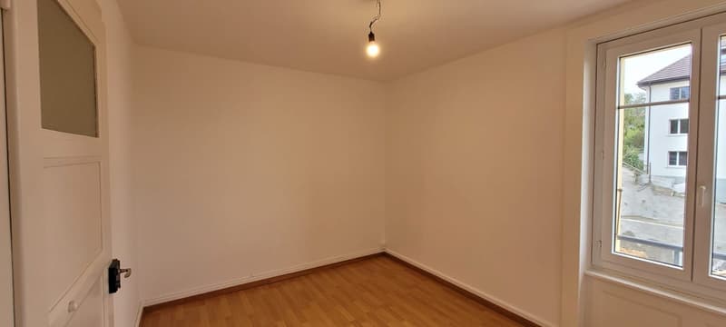Empty room with wooden floor, white walls, two doors, one window with a view.