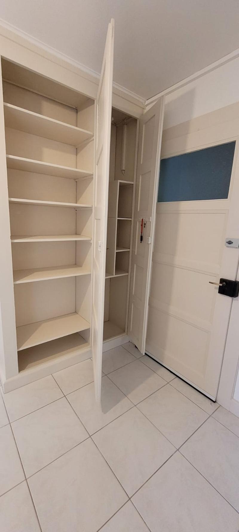 room with a tiled floor, a tall white built-in wardrobe with shelves and a door in the middle, keys on a hook and a white door on the right side.