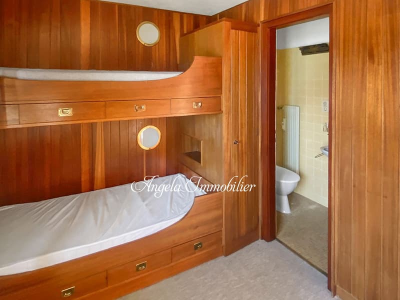 Wooden bunk beds, wooden walls, white bedding, wooden drawers, round porthole, wooden door, bathroom with toilet and radiator