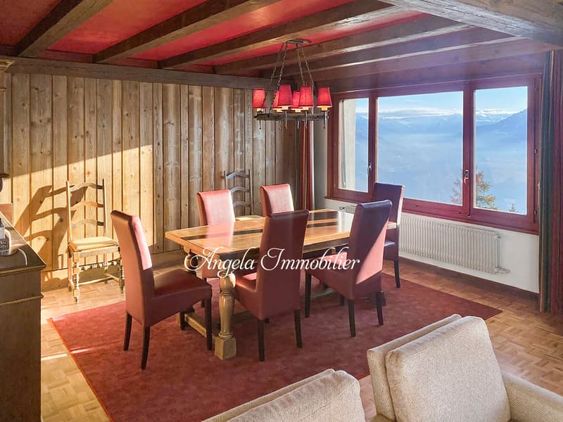 Dining room with wooden walls, wooden table, red chairs, chandelier, carpet, large windows, view of mountains