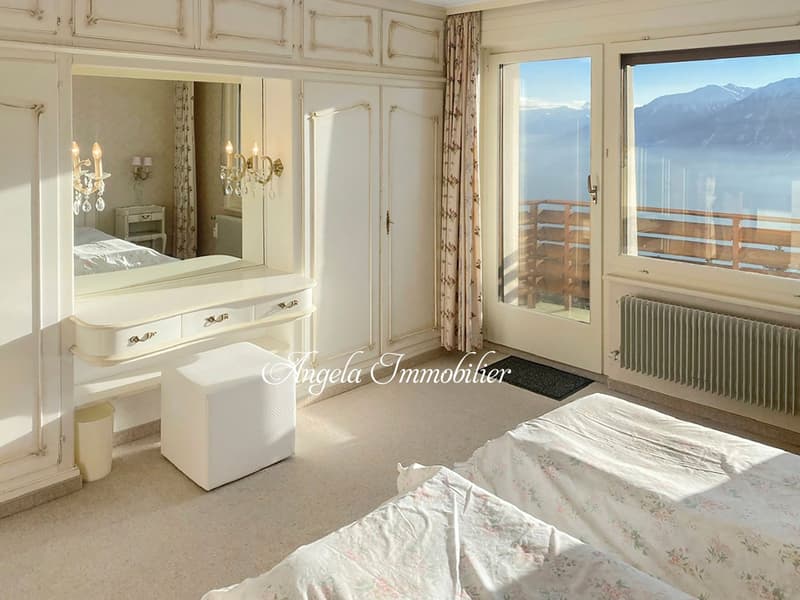 bedroom with two beds, large mirror, white furniture, balcony with railing, mountain view