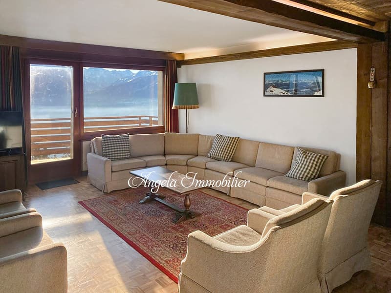 large windows, wooden beams, beige sofa, coffee table, rug, lamp, picture frame, television