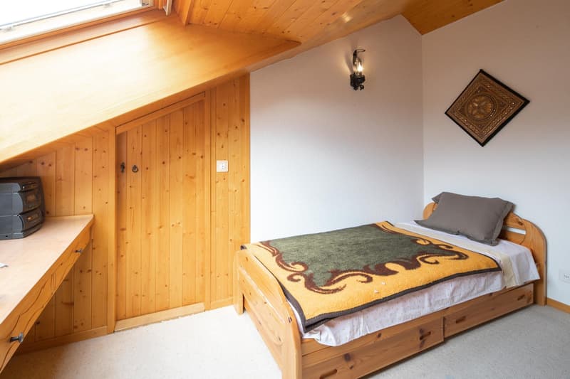 small bedroom with wooden bed, wooden walls, wooden desk, wall lamp, small window, wall art