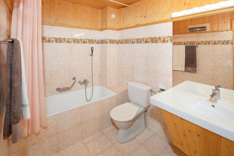 Bathroom with bathtub, toilet, sink, wooden walls, tiled floor, shower curtain, towels, mirror, and faucets.