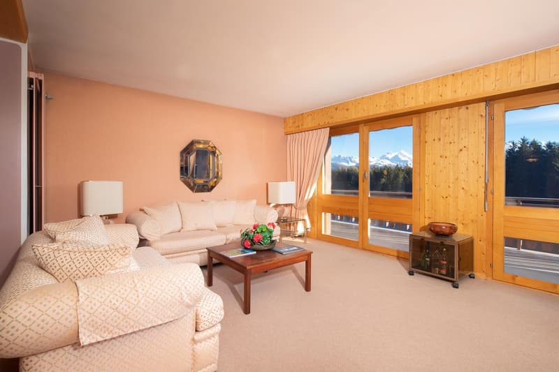 living room with beige couches, wooden coffee table, wooden wall, large windows with view of mountains
