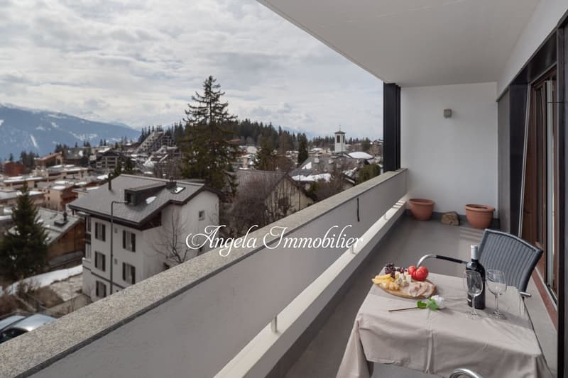 Balcony with table and chairs, view of the town and mountains, wine bottle, wine glasses, food platter