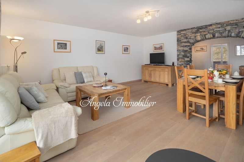 living room with sofa, coffee table, TV, dining table, chairs, lamp, wooden floor, stone wall, wooden cabinet, pictures on the wall