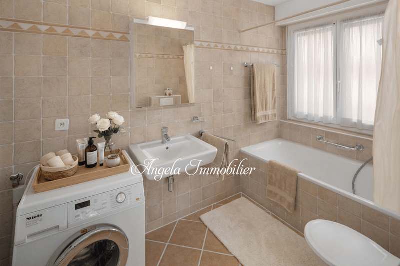 Bathroom with bathtub, sink, toilet, washing machine, mirror, towel rack, and tiled walls.