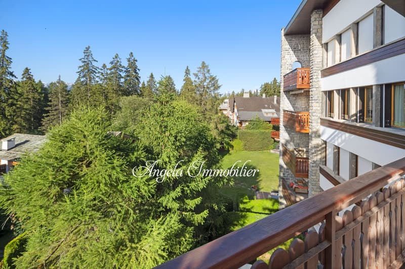 A building with balconies, surrounded by trees and grass, with a clear view of the sky