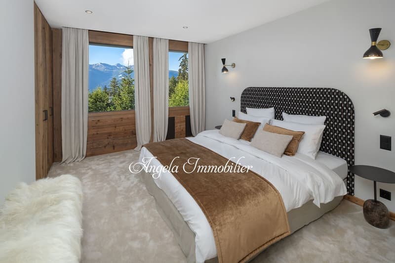 large bed, white and brown bedding, white walls, wooden floor, large windows, white curtains, white fur rug, side table, lamps