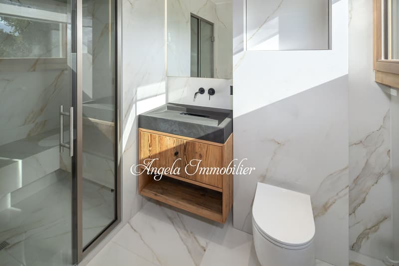 modern bathroom with marble walls, glass shower, wooden cabinet, sink, toilet