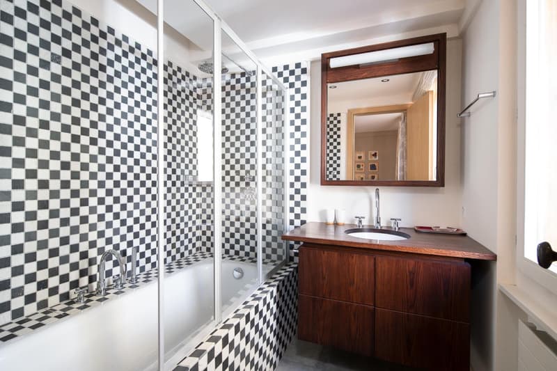 Bathroom with black and white checkered tiles, bathtub, shower, wooden vanity, mirror, and faucet