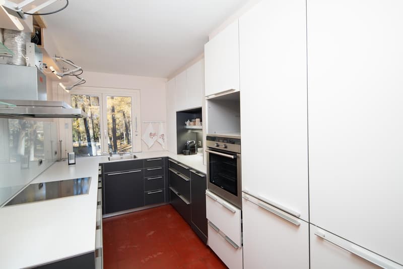 modern kitchen with white cabinets, black countertops, stainless steel appliances, red tiled floor