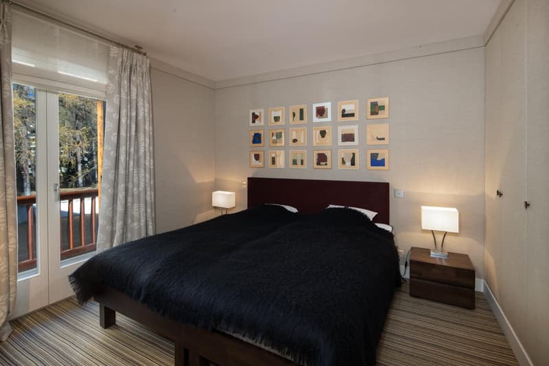 double bed, black blanket, bedside lamps, wall art, balcony, window with curtains