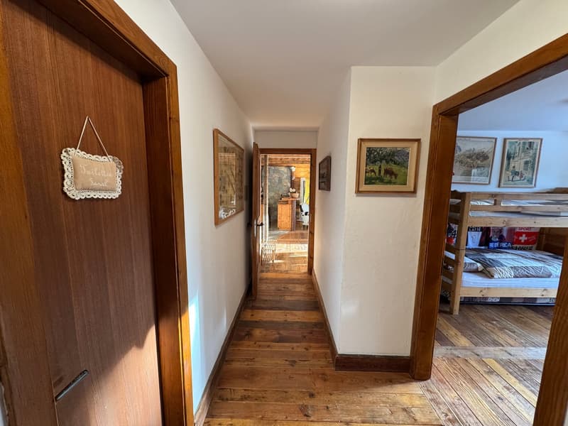 hallway with wooden floor, white walls, wooden door, wooden bunk bed, framed pictures on the wall
