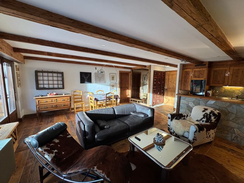 wooden beams, wooden floor, black leather couch, cowhide chair, glass coffee table, wooden cabinet, dining table, chairs, kitchen area, fireplace