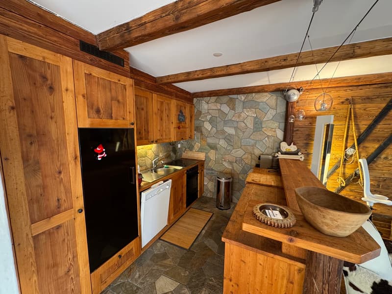 wooden cabinets, granite countertop, black refrigerator, dishwasher, wooden floor, stone wall
