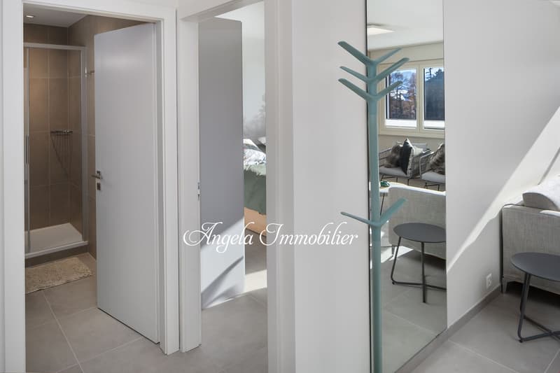 Entrance, bathroom with shower, coat rack, round table, sofa, mirror, open doorway to bedroom with bed, windows