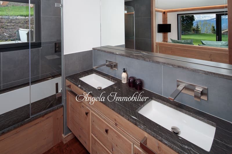 Modern bathroom with gray tile walls, wooden vanity with granite countertop, undermount sink, and a large window overlooking the outdoor landscape