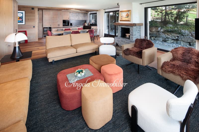 Spacious open-plan living area with wooden walls and floors, large windows, stone fireplace, comfortable sofas and armchairs, coffee table, and a dining area with a table and chairs
