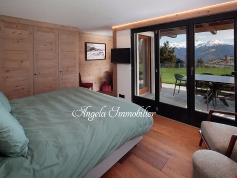 Spacious bedroom with wooden walls and floors, large windows overlooking a balcony or terrace, and a comfortable bed with green bedding.