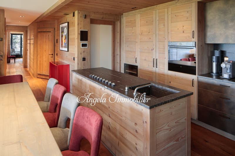 Spacious open-plan kitchen with wooden walls and cabinets, granite countertop, built-in appliances including a dishwasher, and dining area with red upholstered chairs