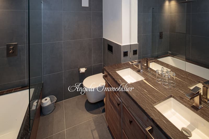 Modern bathroom with dark gray tile walls, wooden vanity with double sinks, and a dishwasher visible on the counter.