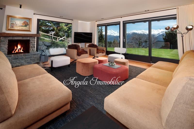 Spacious living room with large windows offering a scenic mountain view, a stone fireplace, comfortable seating including sofas and armchairs, and a coffee table with decorative accents.