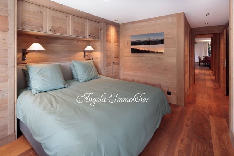 Spacious bedroom with wooden walls and floors, large bed with blue bedding, wall-mounted lamps, and a landscape artwork on the wall