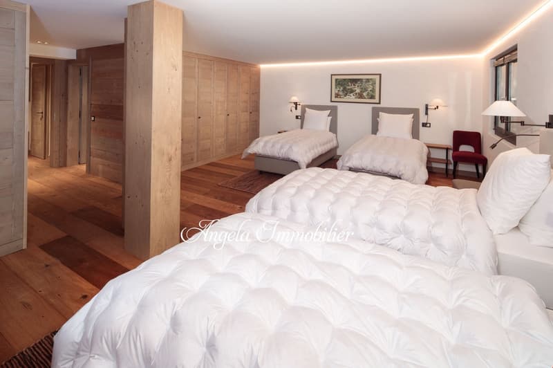Spacious bedroom with wooden floors, wooden built-in wardrobes, two twin beds with white bedding, a red armchair, and a fireplace in the room.
