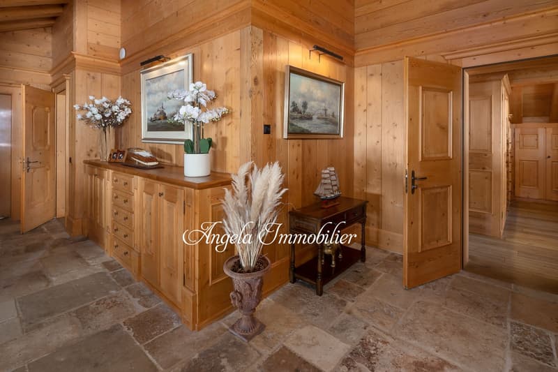 Spacious entryway with wooden walls and floors, decorative vase with flowers, framed artwork, wooden cabinet, and a small table with decor items.