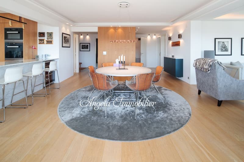large dining table, round, surrounded by 6 chairs, marble countertop, round rug, wooden flooring, chandelier, open kitchen with appliances