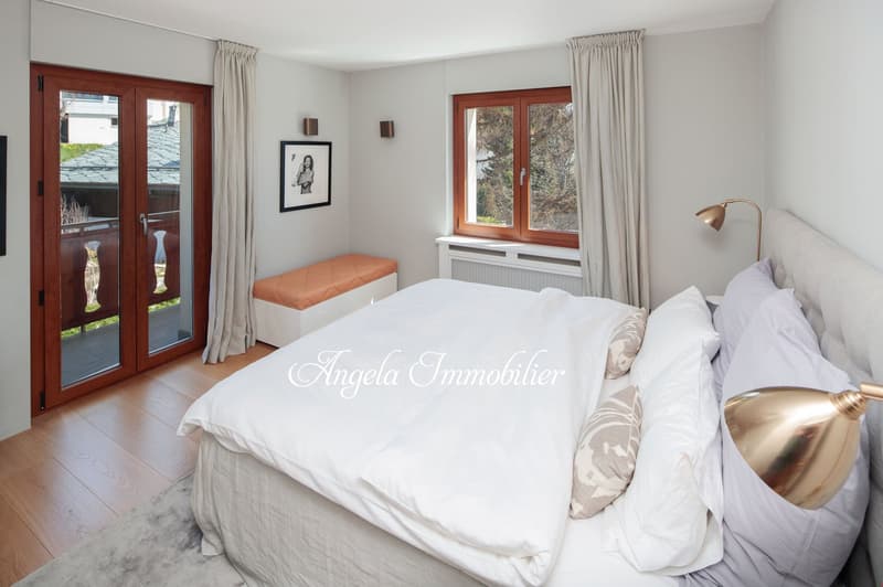 large bed, white bedding, glass doors leading to balcony, brass lamps, framed picture on wall, white radiator, carpet