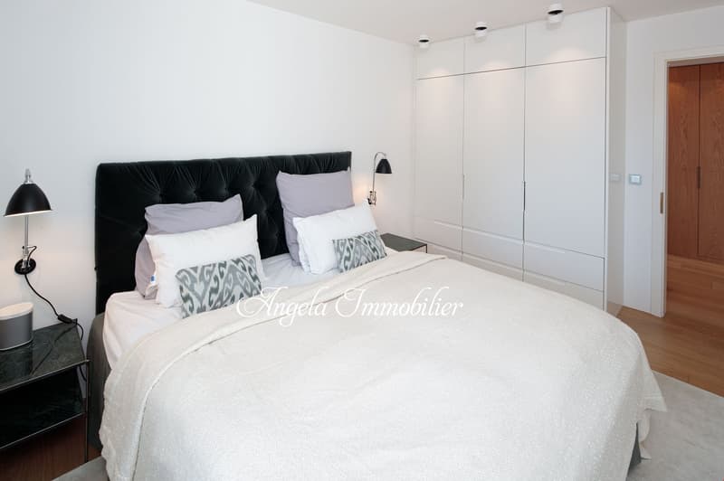 black headboard, white bedding, multiple pillows, bedside lamps, white wardrobes, wooden floor