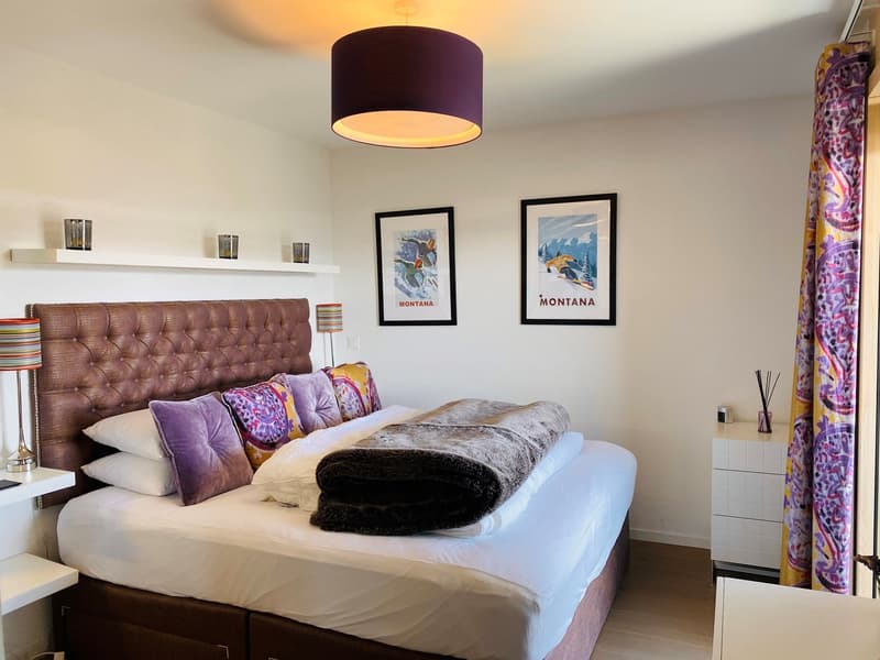 Bedroom with a bed, pillows, blankets, lamps, shelves, framed pictures, and a cabinet