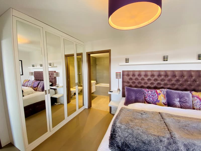 Large bedroom with a bed, a large wardrobe, a mirror, a lamp, a nightstand, a bathroom with a bathtub and a toilet