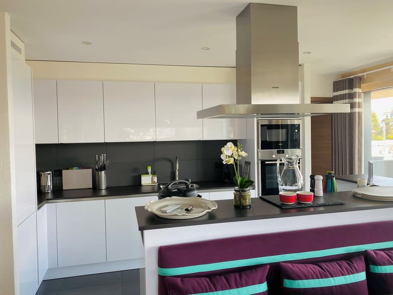 modern kitchen with white cabinets, black countertops, stainless steel appliances, island with seating, large window