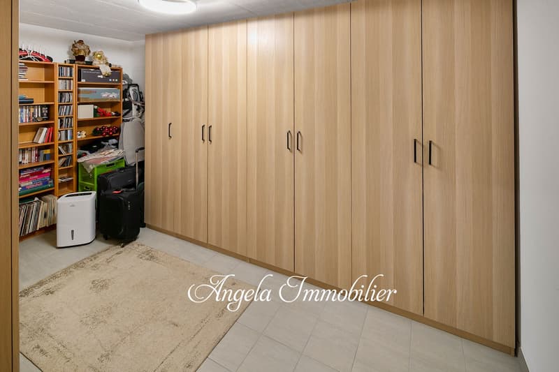 Spacious bedroom with built-in wooden wardrobes, bookshelves, and a dehumidifier. The room has a tiled floor and appears to be well-organized.