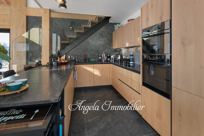 Modern kitchen with wooden cabinets, black countertops, built-in appliances including a dishwasher, and a slate tile backsplash. The kitchen also features a staircase and shelving units.