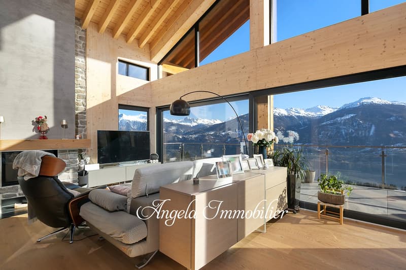Spacious living room with large windows offering a panoramic view of the snowy mountains, wooden beamed ceiling, modern furniture including a sofa and armchair, TV, and decorative items on a sideboard.