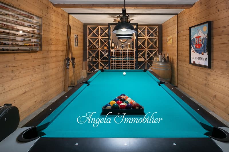 Spacious game room with a pool table, wooden walls and ceiling, wine cellar, and a fireplace. The room also features a chandelier and artwork on the walls.