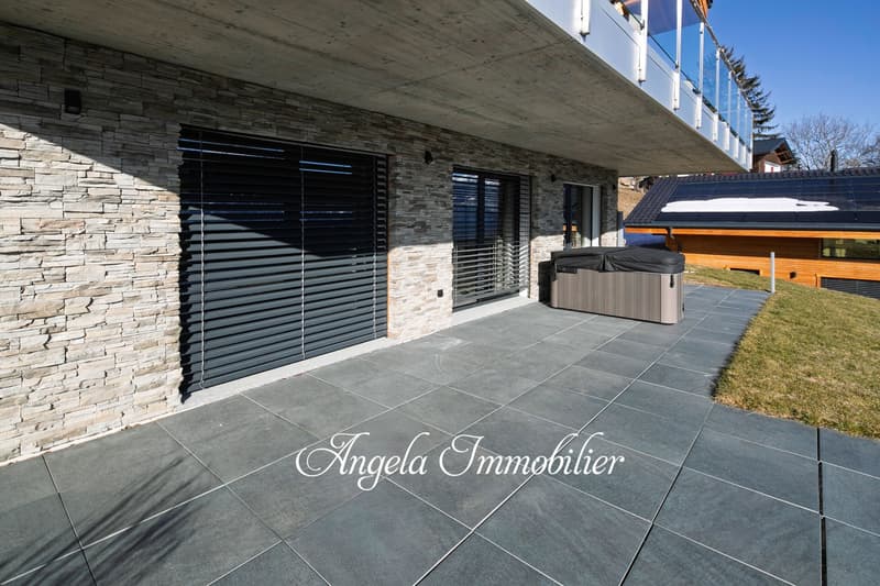 Two-story commercial building with a stone facade, large windows, and a covered outdoor terrace area. The building has a sign for 'Angela Immobilier' on the ground floor.