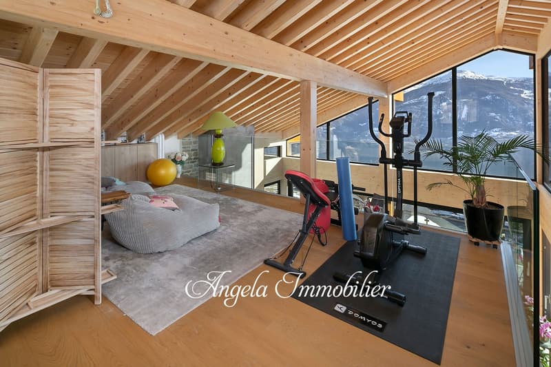 Spacious bedroom with wooden beamed ceiling, large windows offering a scenic mountain view, exercise equipment, and a cozy seating area.