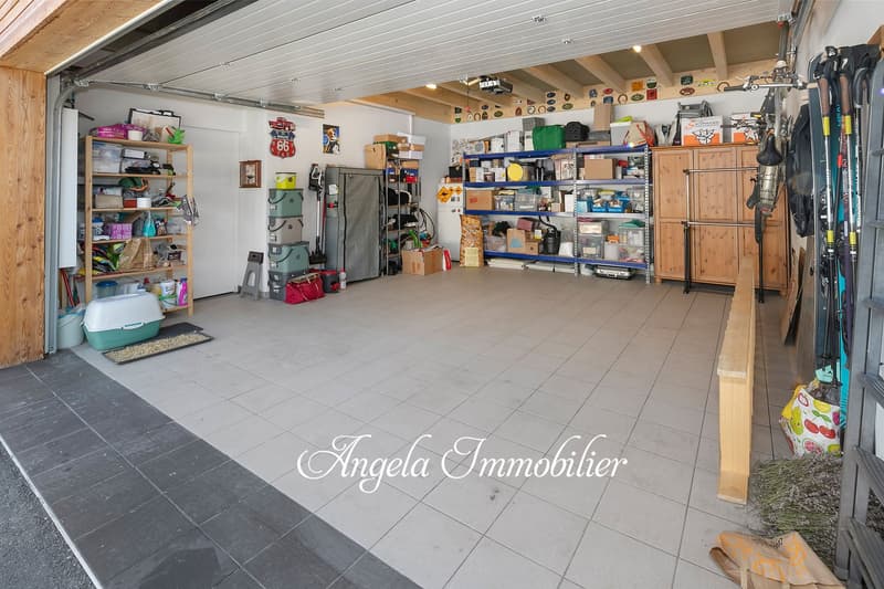 Spacious garage with tiled flooring, wooden shelves and storage units, various household items and equipment stored, and a garage door visible.