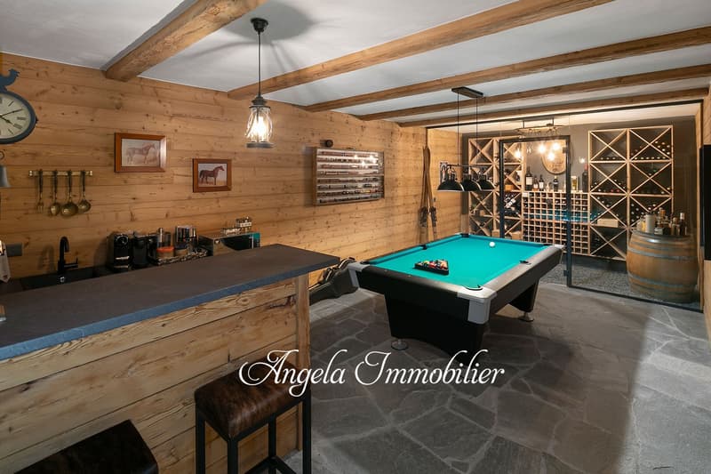 Rustic wooden walls and ceiling with exposed beams, pool table, wine rack, bar counter, and hanging light fixtures