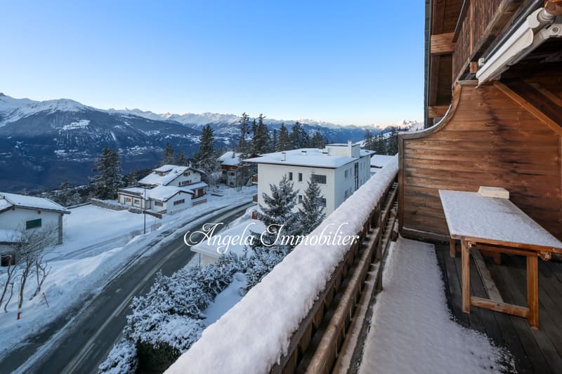 wooden balcony, snow-covered ground, wooden table, snowy mountains in the background