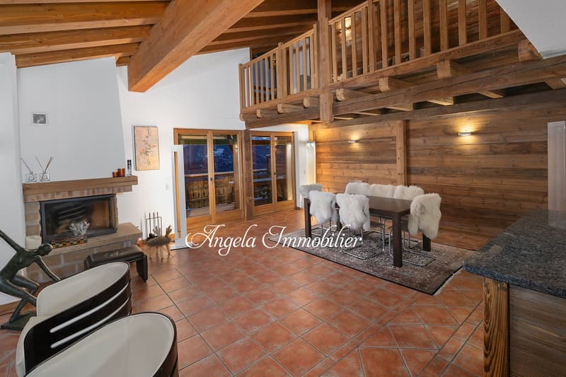 Large open-concept living space with wooden beams, exposed wood walls, tiled floor, fireplace, dining table with fur-covered chairs, and glass doors leading to an outdoor area.