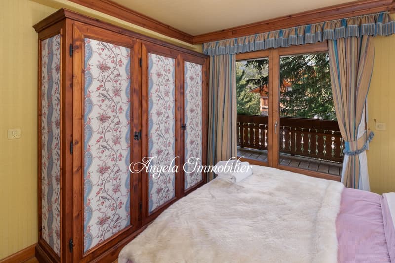 Spacious bedroom with wooden wardrobe, floral patterned curtains, balcony with wooden railing, and a view of the surrounding trees