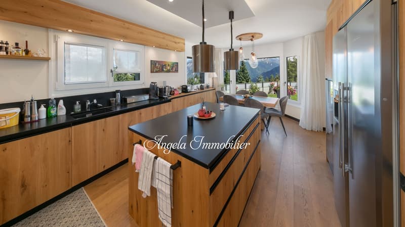 Spacious open-concept kitchen with wooden cabinetry, black countertops, pendant lighting, and a large window overlooking a scenic mountain view.